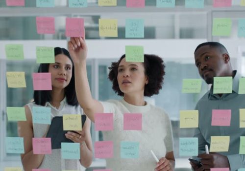 Business people, collaboration and sticky notes on glass board for data analytics, planning ideas and teamwork. Creative team, women and men with digital tablet, brainstorming or SEO for social media